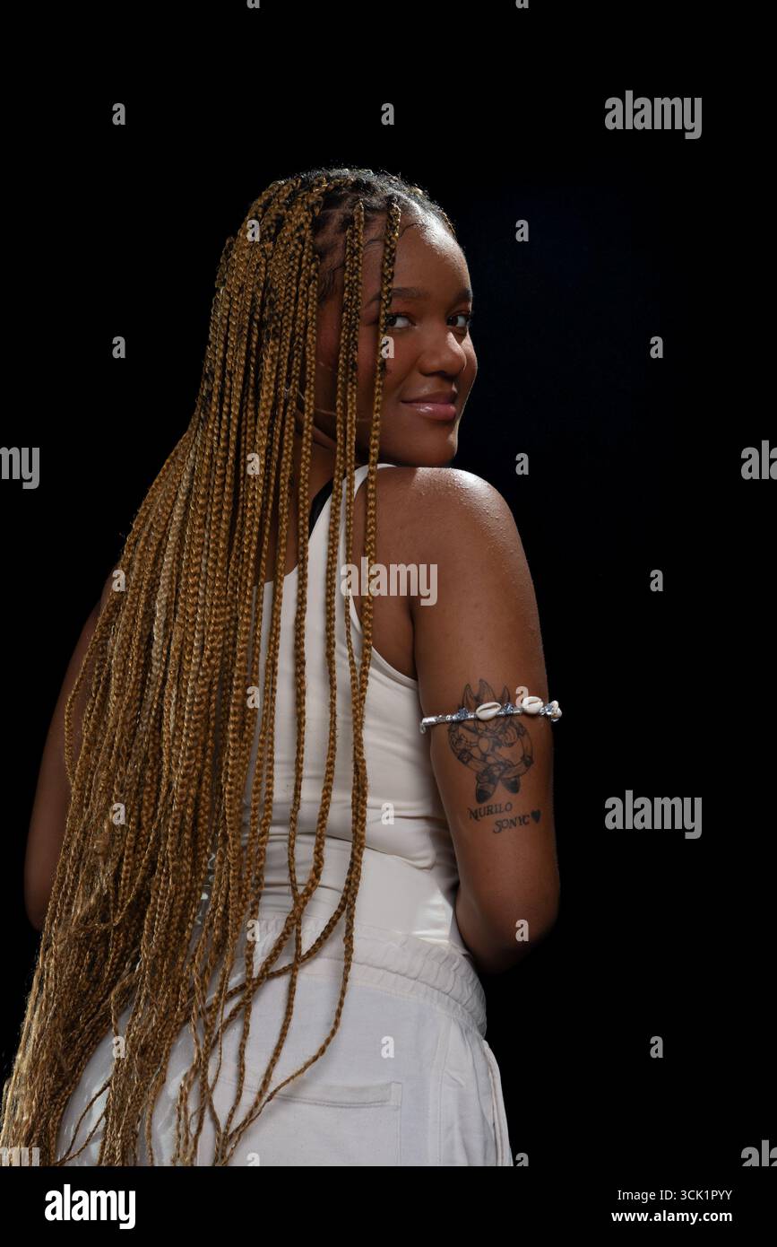 Salvador, Bahia, Brasilien - 30. August 2025: Junge Frau mit geflochtenem Haar, die mit dem Rücken zur Kamera steht und für ein Studiofoto gegen einen Blac posiert Stockfoto