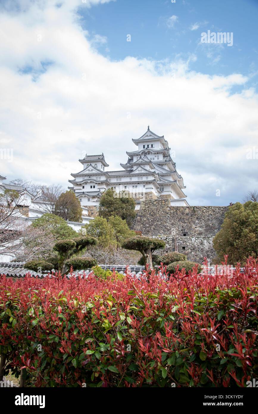 Himeji Castle mit roten Sträuchern im Vordergrund. Himeji Castle mit roten Sträuchern und Frühlingsgrün in Hyogo, Japan. Stockfoto