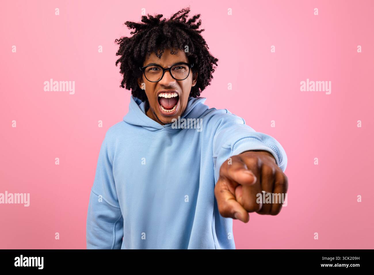 Wütender schwarzer Teenager, der auf rosafarbenen Studiohintergrund schrie und auf die Kamera zeigte. Konzept der negativen Emotionen Stockfoto