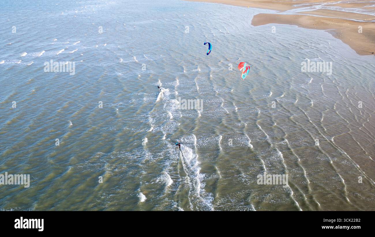 Zwei Kitesurfer mit farbenfrohen Kitesurfern rasen über das Wasser in der Nähe des Strandes. Kleine Wellen und konstanter Wind schaffen perfekte Bedingungen für Wassersport Stockfoto