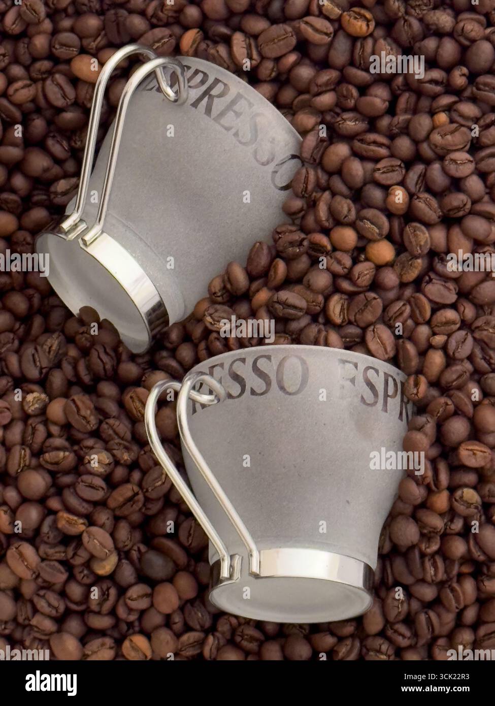 Eine Hochwinkelaufnahme von zwei Espresso-Tassen, die auf einem Bett mit gerösteten Kaffeebohnen liegen. Das Bild hebt die Textur und die tiefbraune Farbe der Bohnen hervor, weiß - Smartphone-aufgenommenes Stockfoto