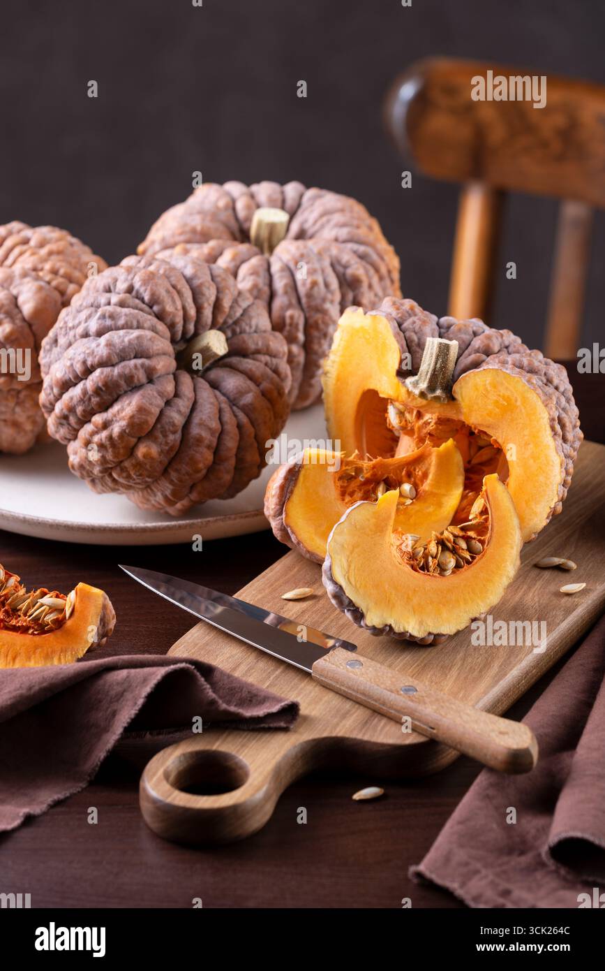 Schwarzer Futsu-Kürbis mit leuchtend orangefarbenem Fleisch und Keilen auf Einem Küchentisch, bereit zum Kochen Stockfoto