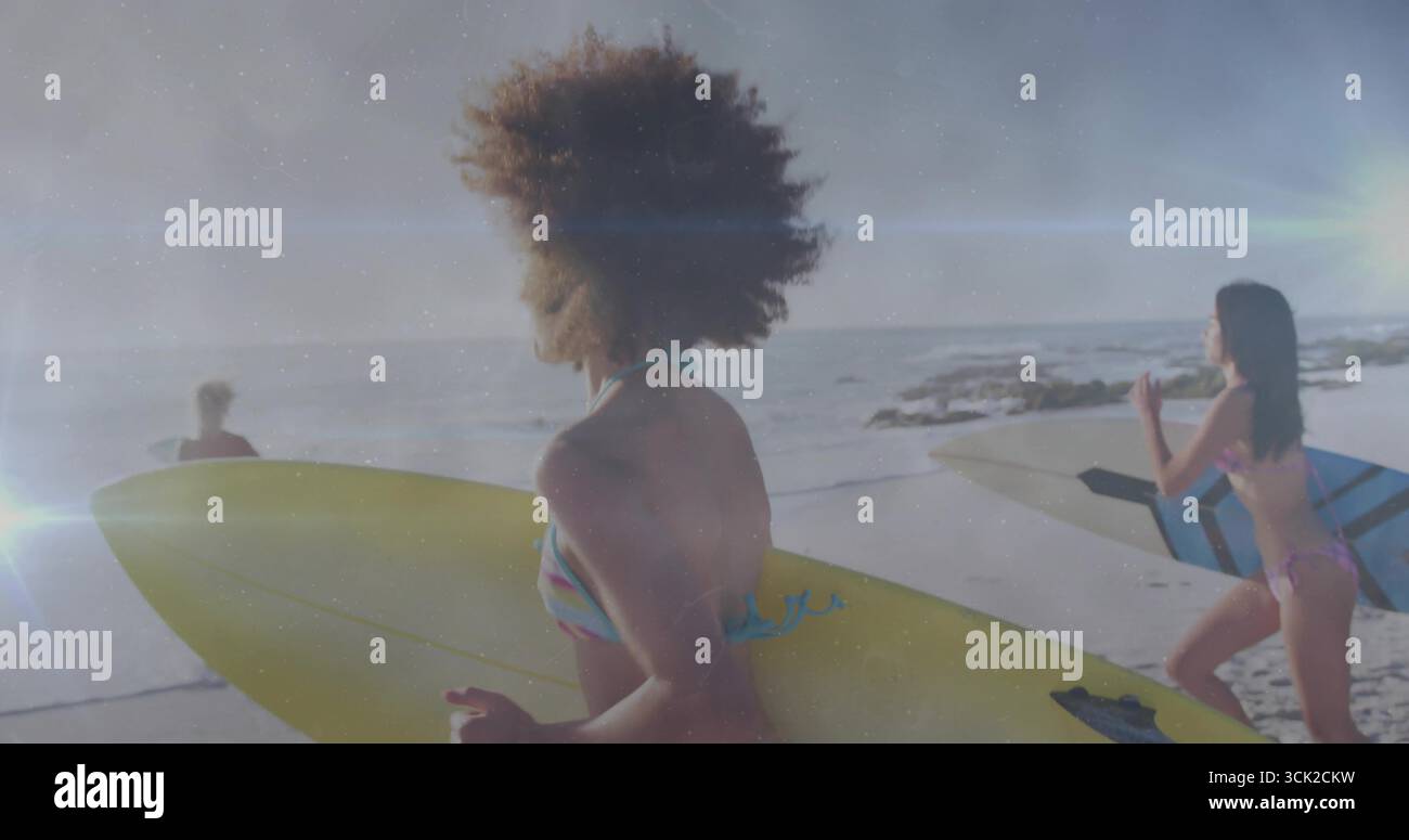 Drei Frauen in Bikinis mit Surfbrettern am Sandstrand bei Sonnenuntergang, Meereswellen Stockfoto