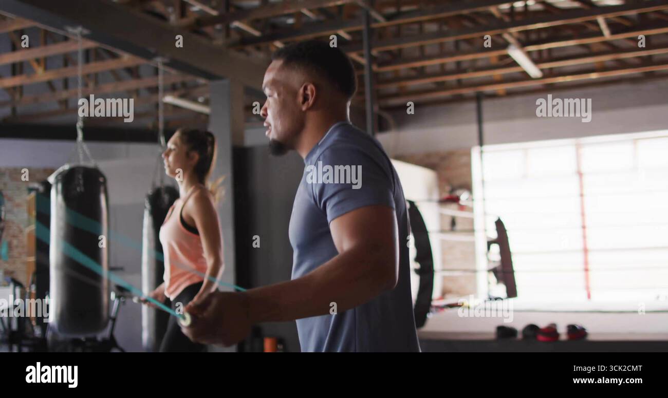 Überspringen von Trainingspartnern, die Sprungseile in der Boxhalle halten und Boxsäcke und Ringseile zeigen Stockfoto
