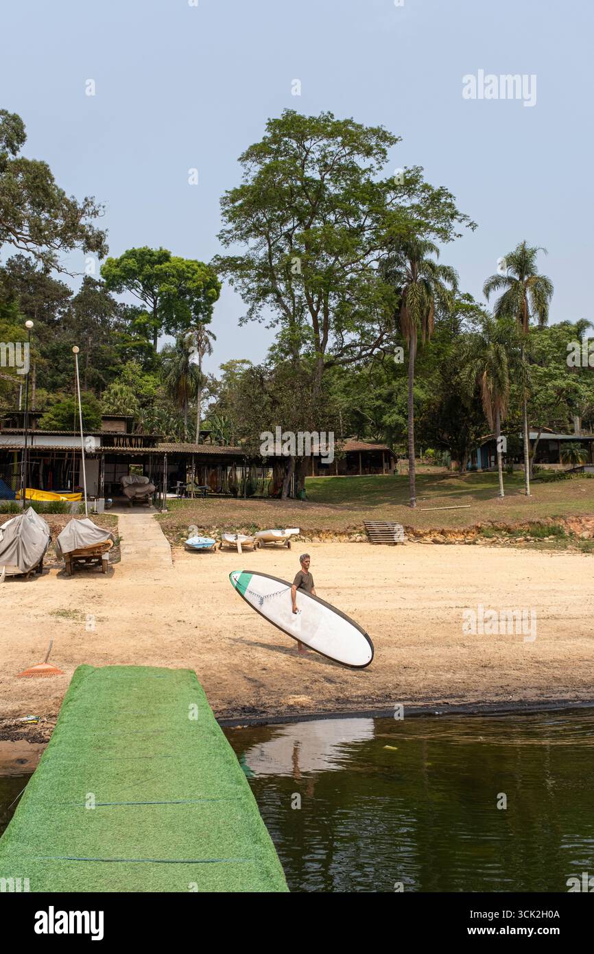 54-jähriger brasilianischer Mann am Rand des Guarapiranga-Damms mit einem Stand-up-Paddleboard vertikal. Stockfoto