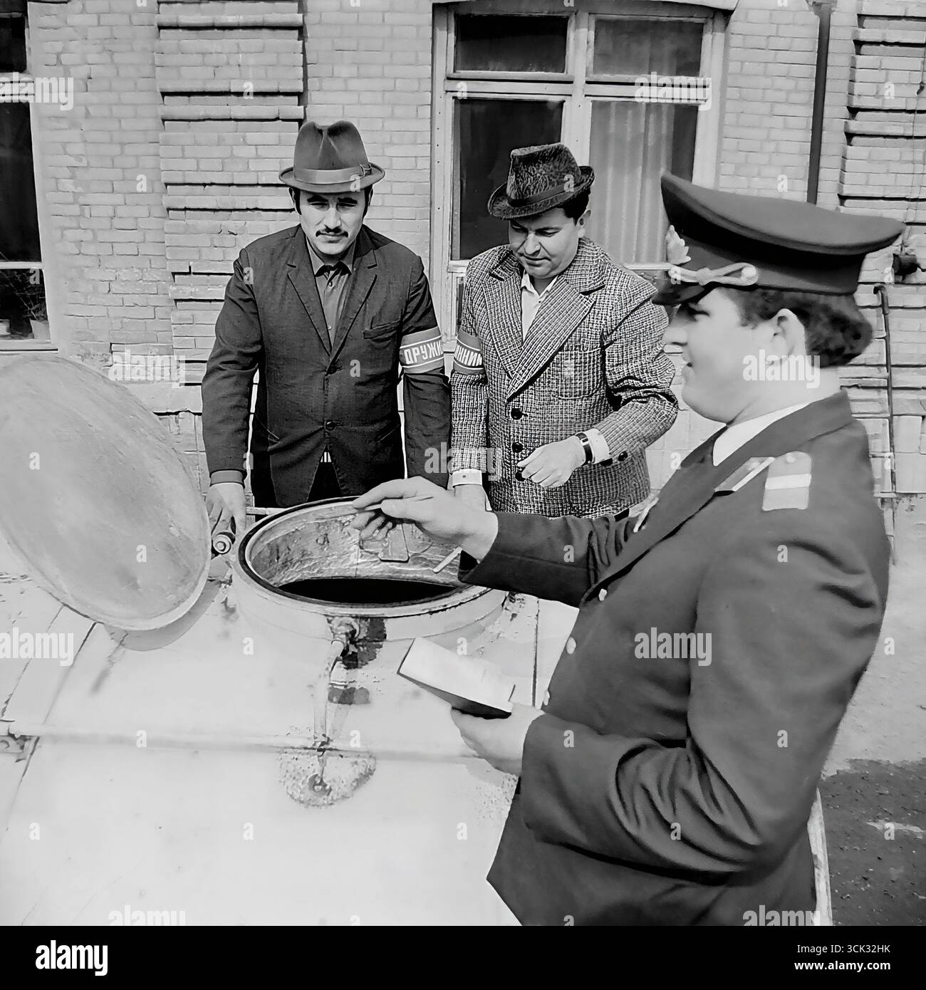 Ein Angriff auf Mondschein in Sloviansk, ukrainische SSR, in den 1980er Jahren Das Archivfoto zeigt einen Militsiya-Offizier in Anwesenheit zweier Druzhinniks, die als offizielle Zeugen fungieren, und inspiziert den Inhalt eines Fasses, das vermutlich Maische oder Mondschein enthält. Diese Szene ist ein dokumentarischer Beweis für den Kampf gegen Wirtschaftsverbrechen und Verstöße gegen die öffentliche Ordnung in der späten UdSSR, an der die freiwilligen Volksdruschinen (DND) aktiv beteiligt waren Stockfoto