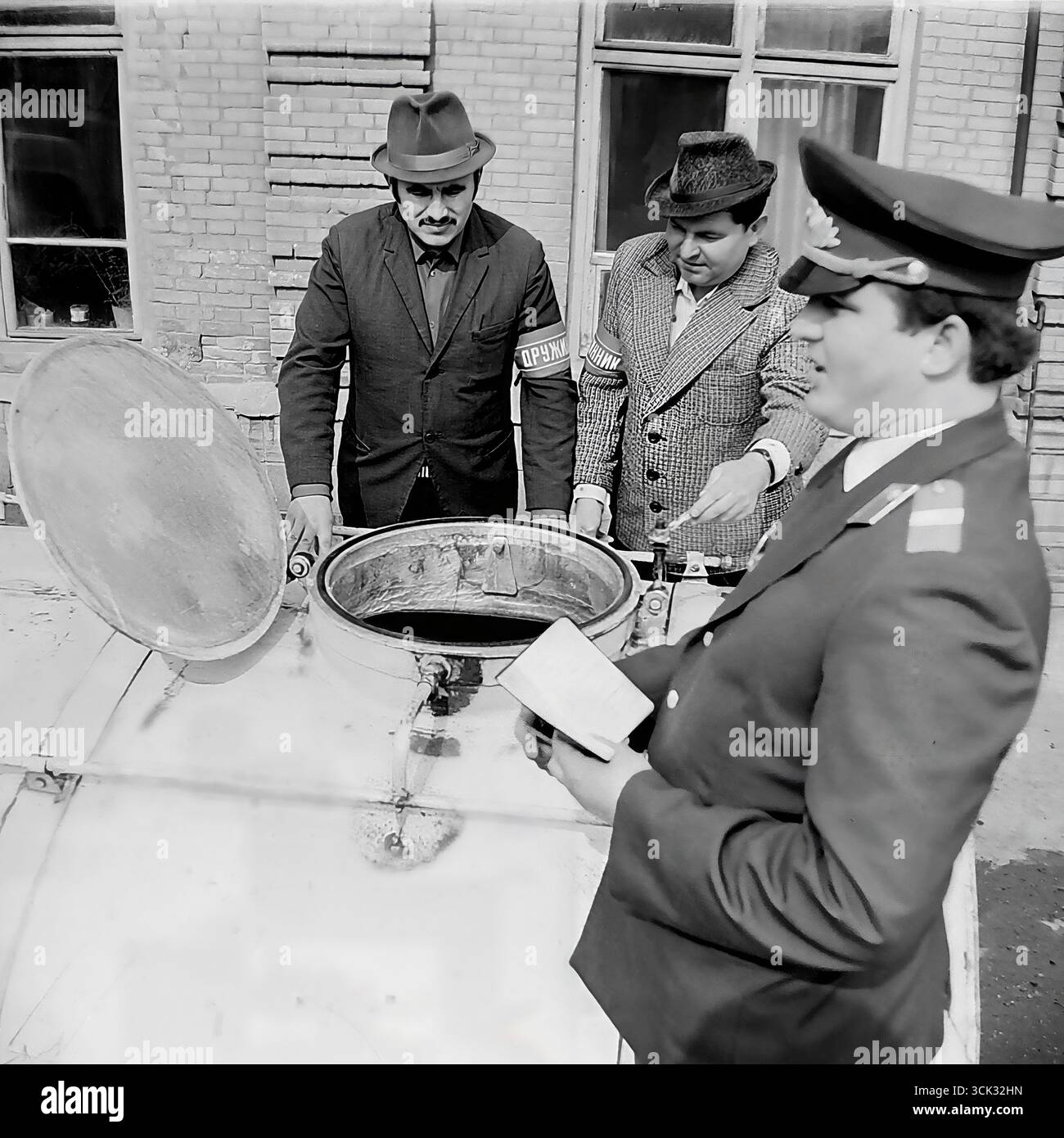 Ein Angriff auf Mondschein in Sloviansk, ukrainische SSR, in den 1980er Jahren Das Archivfoto zeigt einen Militsiya-Offizier in Anwesenheit zweier Druzhinniks, die als offizielle Zeugen fungieren, und inspiziert den Inhalt eines Fasses, das vermutlich Maische oder Mondschein enthält. Diese Szene ist ein dokumentarischer Beweis für den Kampf gegen Wirtschaftsverbrechen und Verstöße gegen die öffentliche Ordnung in der späten UdSSR, an der die freiwilligen Volksdruschinen (DND) aktiv beteiligt waren Stockfoto