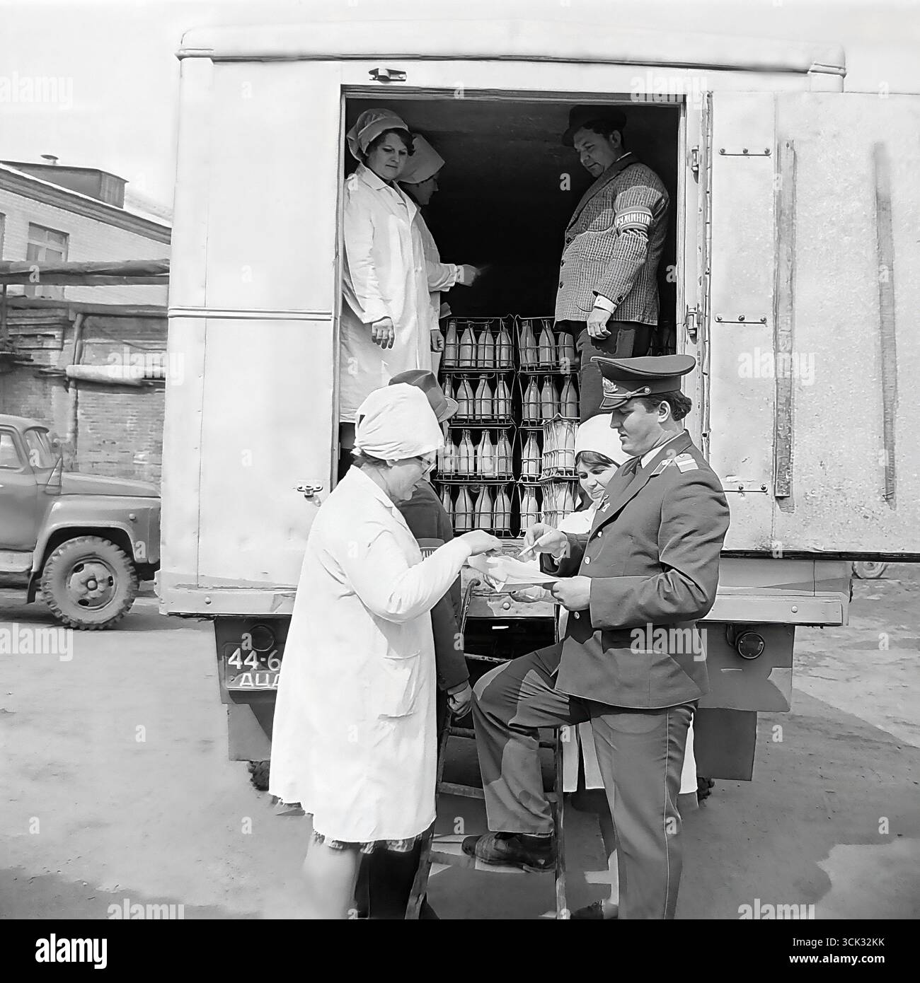 Ein Angriff gegen den Diebstahl sozialistischer Grundstücke in Sloviansk, der ukrainischen SSR, in den 1980er Jahren Das Archivfoto zeigt einen Militsiya-Offizier und einen Druzhinnik (Mitglied der Volkspatrouille), der Dokumente für eine Lieferung von Milchprodukten mit weiblichen Arbeitern aus einem Milchbetrieb überprüft. Diese Szene ist ein eindrucksvolles Dokument der späten UdSSR-Ära, das die Versuche des Staates widerspiegelt, den Warenfluss zu kontrollieren und mit Hilfe von Strafverfolgungsbehörden und der Öffentlichkeit gegen Diebstahl zu kämpfen (DND). Stockfoto