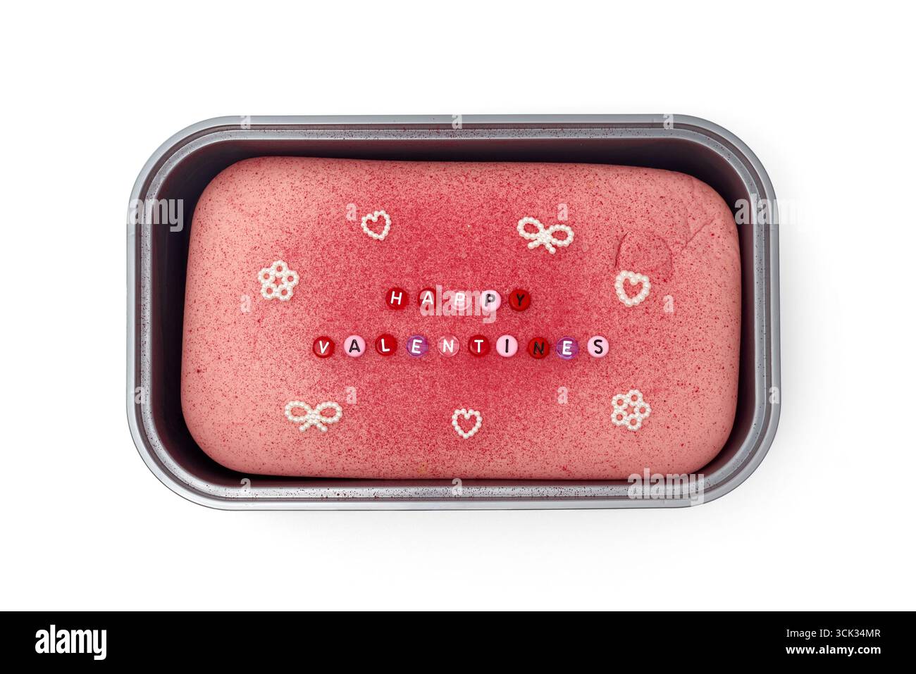 Ein festlicher rosafarbener Kuchen wird mit bunten Bonbons gekrönt, in denen Happy Valentine's geschrieben wird Es wird in ein Backblech gelegt, perfekt für einen Valentinstag-Gat Stockfoto