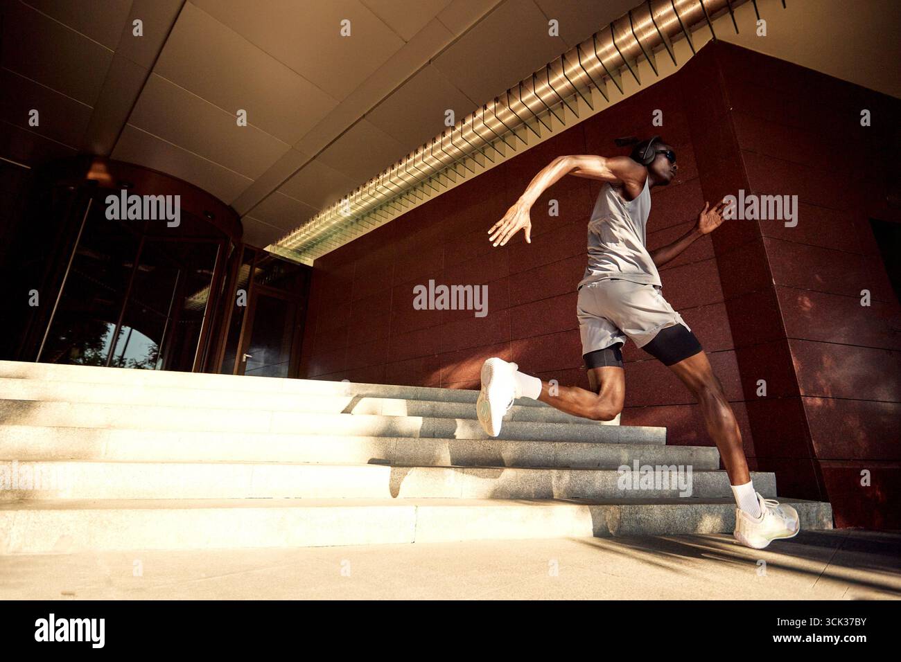 Eine motivierte Person demonstriert körperliche Fitness und Engagement, indem sie eine Treppe in der Nähe eines modernen Gebäudes hinaufspringt. Das Bild erfasst Bewegungen und Stockfoto