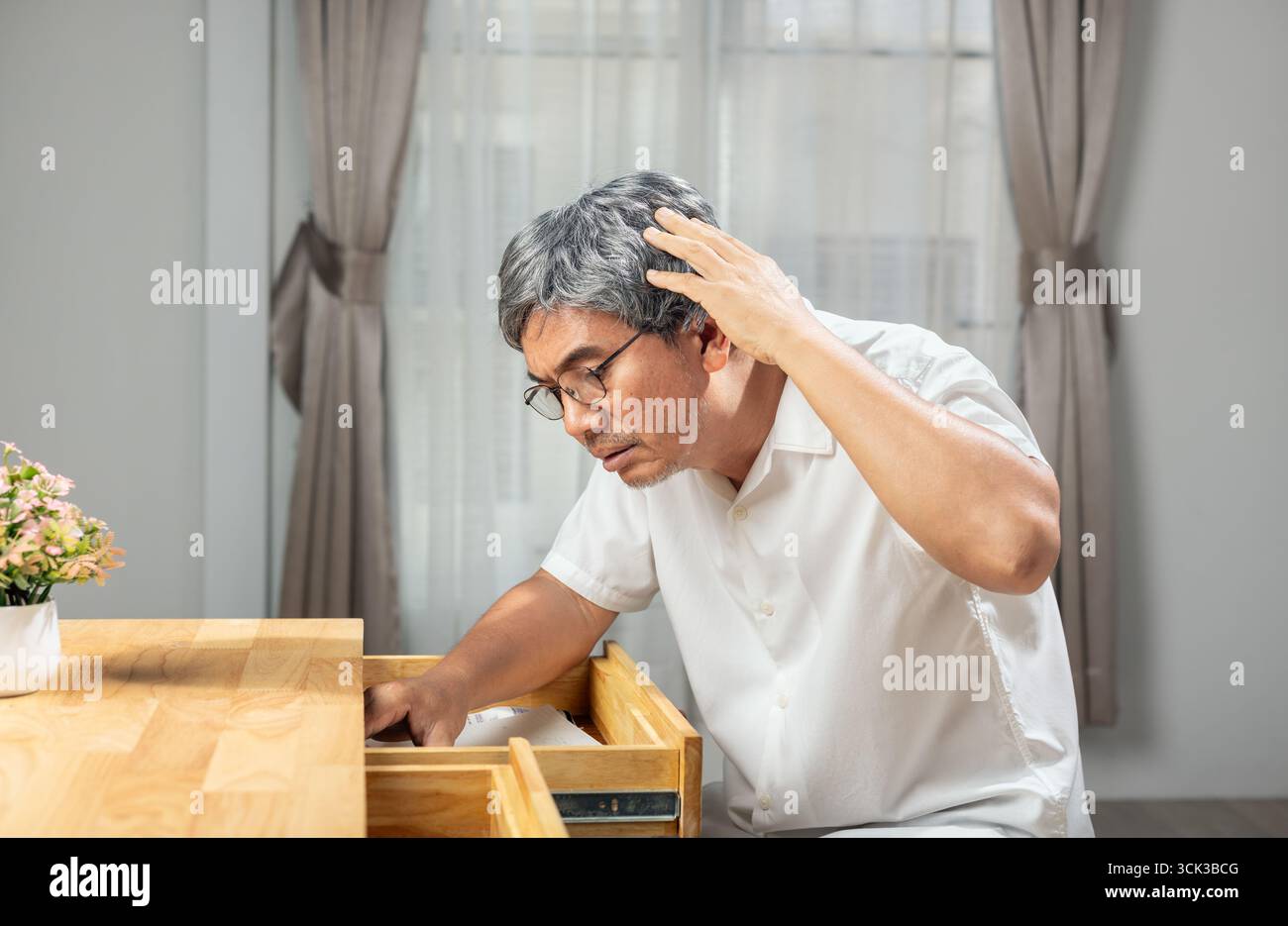 Ein älterer asiatischer Mann findet etwas, das er in den Schubladen vergessen hat. Stockfoto