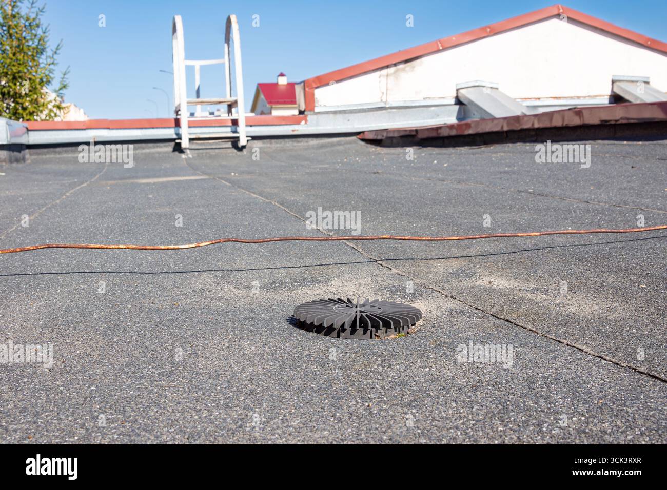 Ein kreisförmiges Kunststoffabflussgitter, das auf einer flachen Dachfläche mit Schotterschutzschicht installiert ist und für eine effiziente Regenwasserableitung mit selekti entwickelt wurde Stockfoto