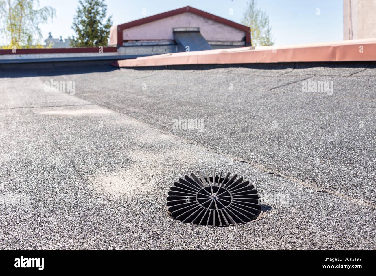 Eine Nahaufnahme eines funktionalen Regenwasserrostes auf einem Flachdach, das mit Bitumenmembran und Kies bedeckt ist, unterstreicht die Bedeutung der Saison i Stockfoto