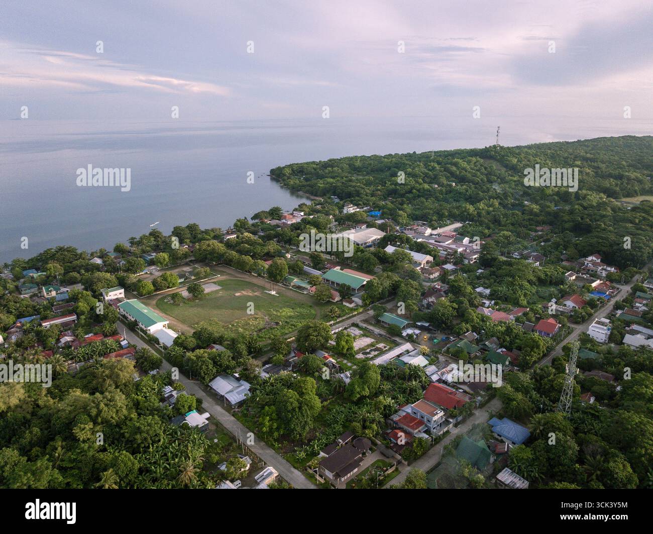 Aus der Vogelperspektive auf die Küste trifft auf das üppig grüne Land, gespickt mit Gebäuden und Bäumen, unter einem weichen Himmel, Lage entfallen. Stockfoto