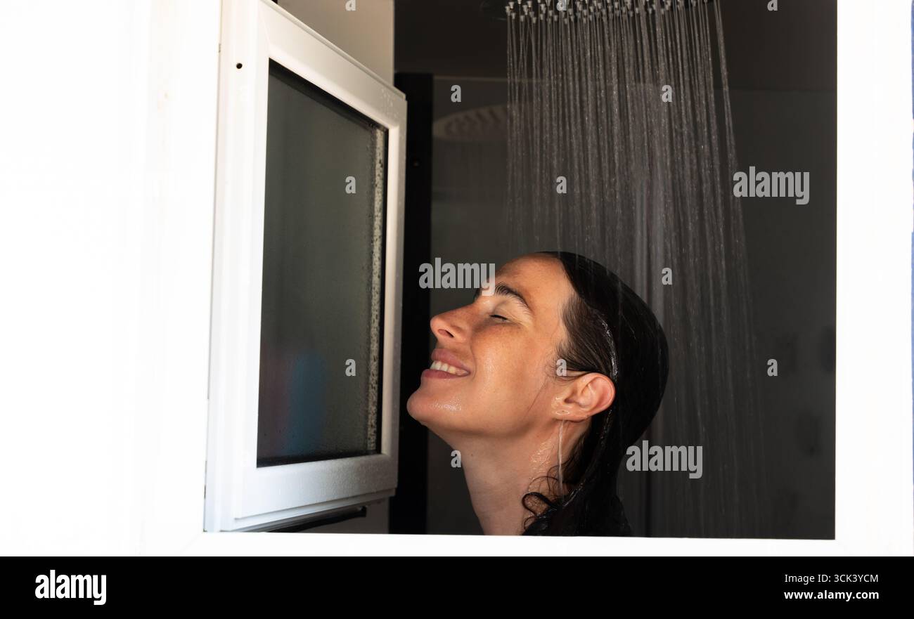 Frau genießt eine erfrischende Dusche im modernen Badezimmer mit geschlossenen Augen Stockfoto