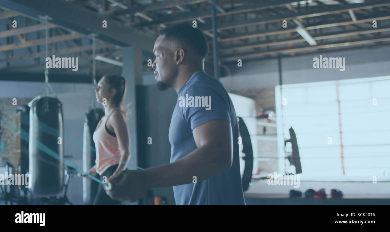 Ein Mann, der ein marineblaues T-Shirt und Shorts trägt, hält ein Sprungseil in der Boxhalle, mit Boxsäcken Stockfoto