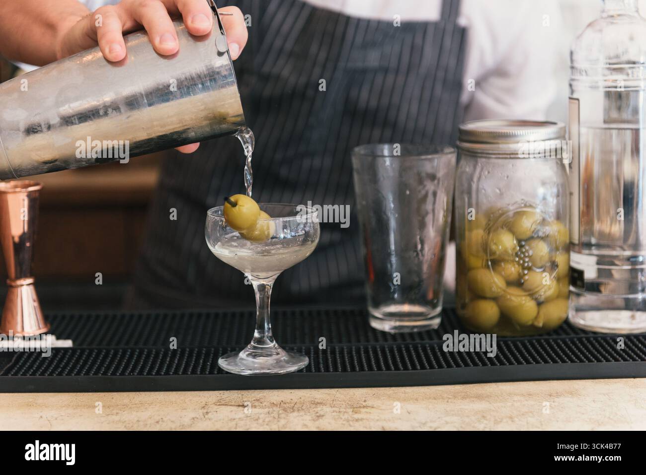 Der Barkeeper gießt Martini aus dem Shaker ins Glas Stockfoto