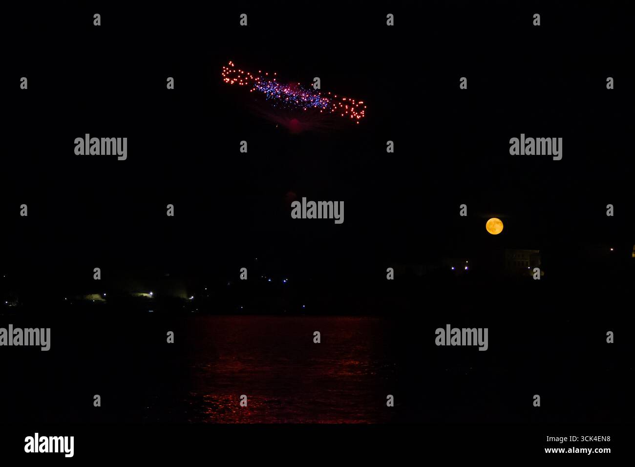Nachthimmel mit Feuerwerk, Vollmond und ruhigen Reflexen auf dem Wasser Stockfoto
