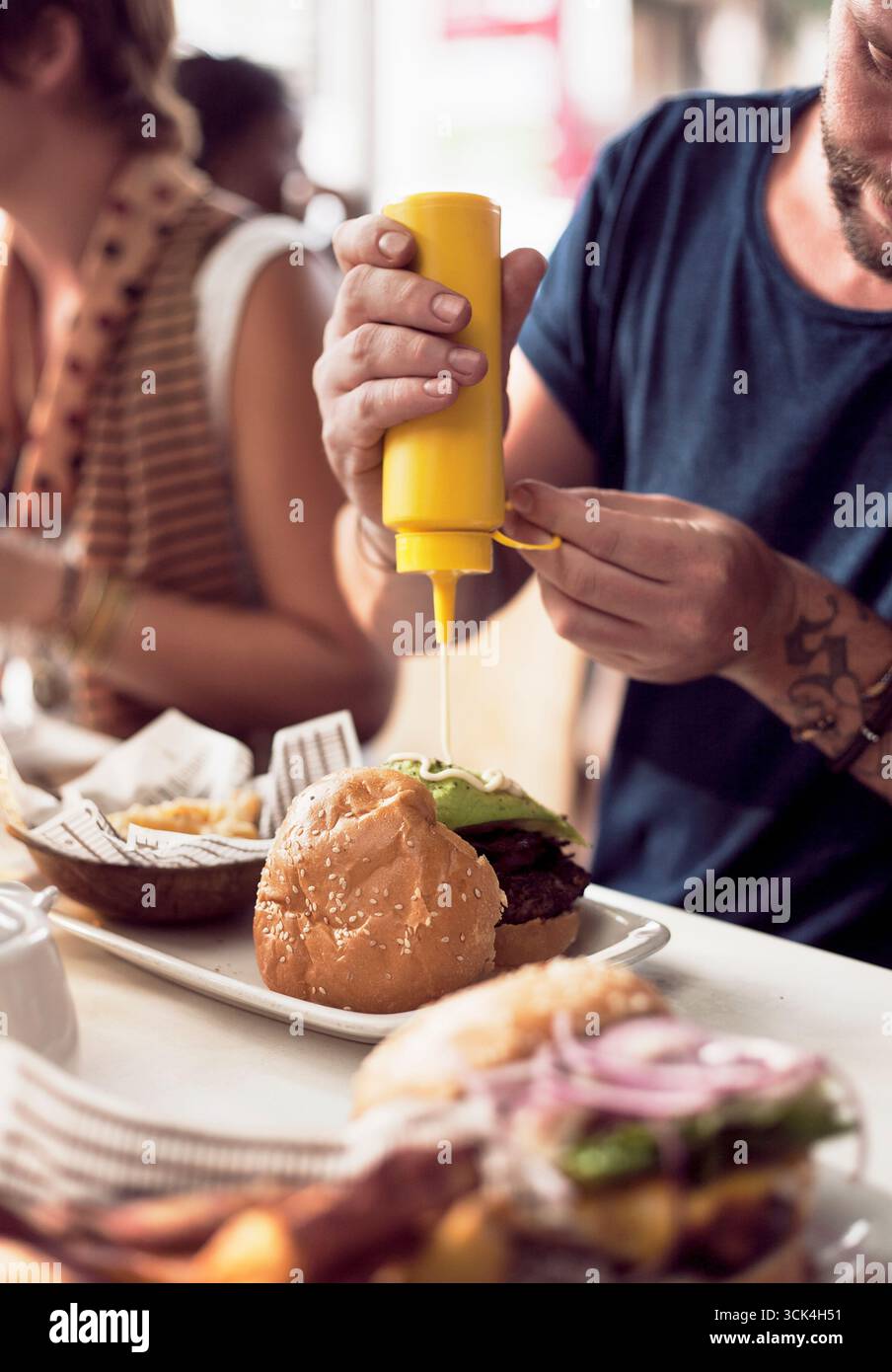 Zugeschnittene Aufnahme von Paaren, die Mayonnaise auf Burger im Straßencafé stecken. Das Bild wurde am 11.01/17 um 12:24 Uhr heruntergeladen Stockfoto