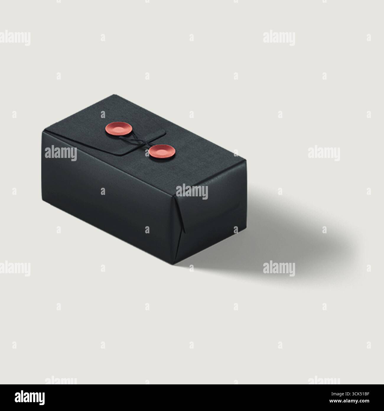 Ein kleines, elegant verpacktes schwarzes Paket mit zwei roten Knöpfen, das ein Geschenk oder einen besonderen Gegenstand andeutet. Stockfoto