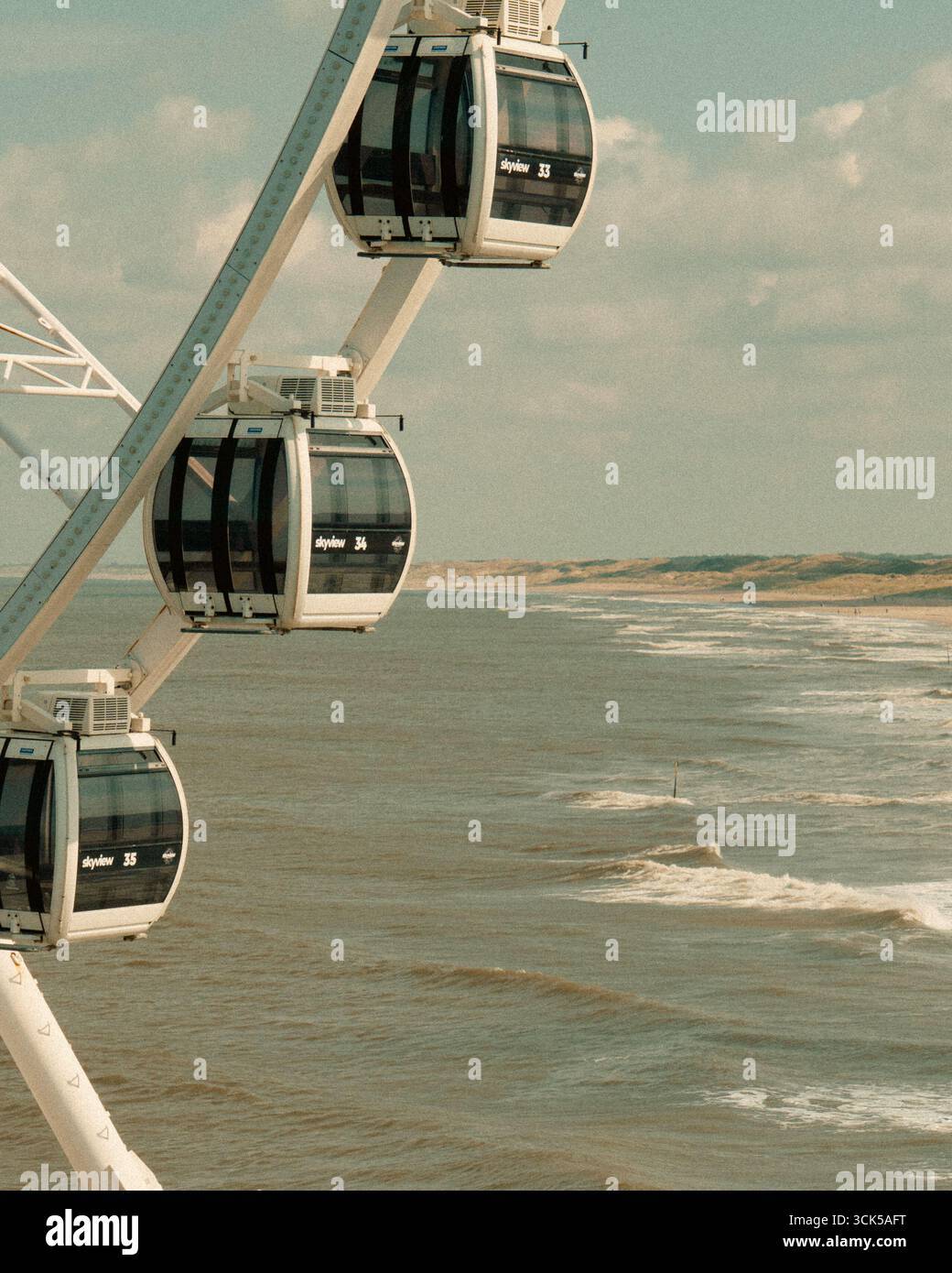 Riesenradkabinen Küstenwellen Sommerblick mit SkyView-Aussichtsrad über dem Meereswasser und malerischer Küstenlandschaft bei weichem Tageslicht Stockfoto