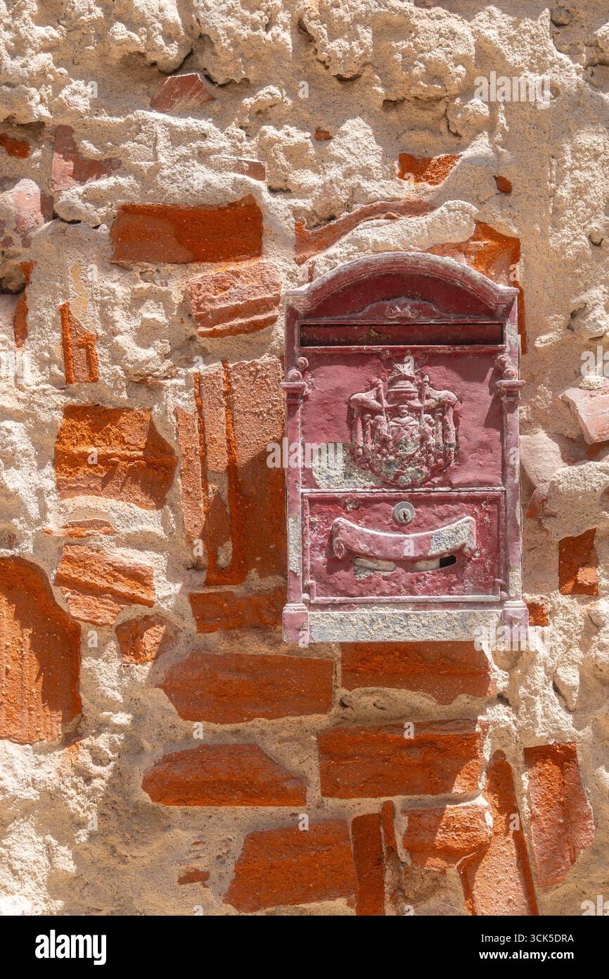Roter Vintage-Briefkasten an einer strukturierten Ziegelwand mit komplexen Details und historischem Charme. Der verwitterte Backsteinhintergrund hebt hervor Stockfoto