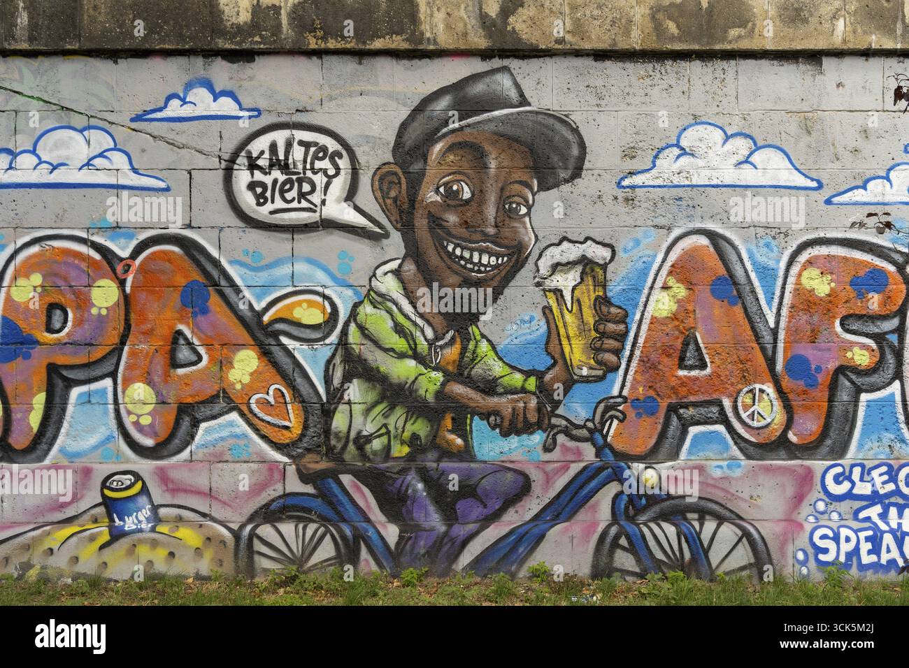 Fröhlicher Mann auf Fahrrad mit Bierflasche, umgeben von kreativen Graffiti und Wolken, am Donaukanal Innere Stadt Wien Österreich Stockfoto