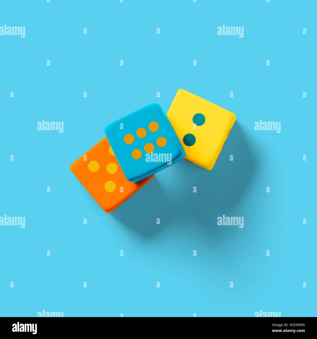 Drei bunte Würfel in Orange, Blau und Gelb mit verschiedenen Punktmustern, ideal für Spiele und Freizeitaktivitäten. Stockfoto