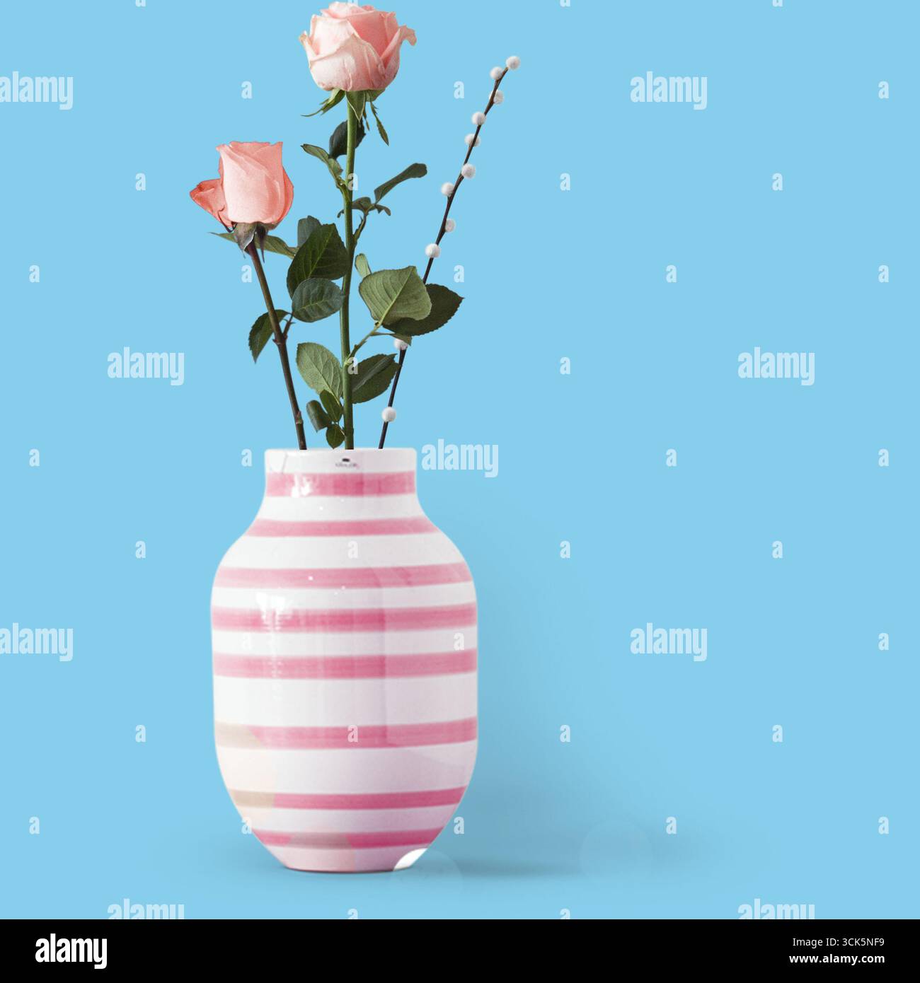 Eine gestreifte Vase mit rosa Rosen und Grün, die als dekoratives Herzstück dient. Stockfoto