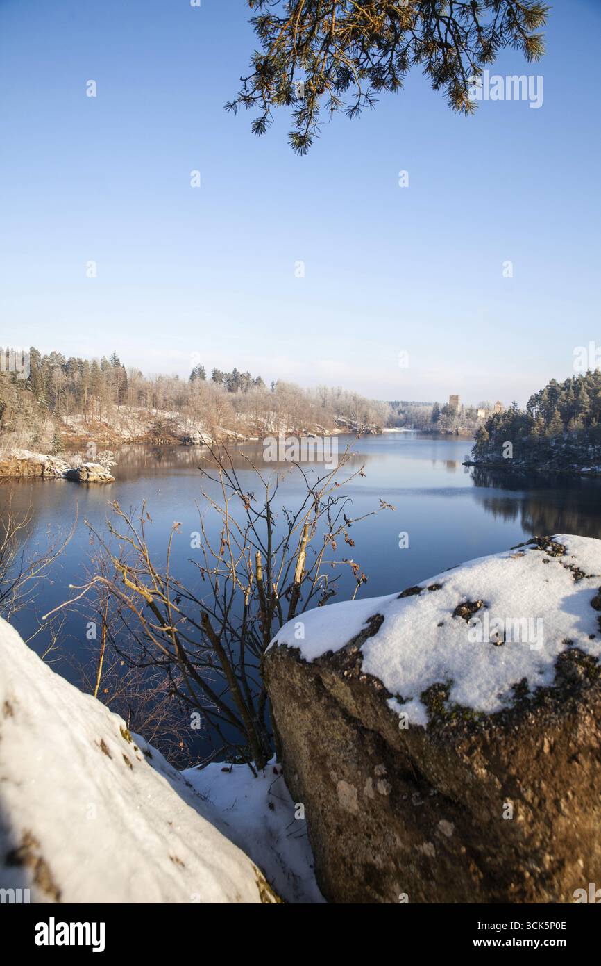 Schneebedeckte Felsen und Bäume umrahmen einen ruhigen See unter klarem blauen Himmel Ottensteiner Stausee Waldviertel Niederösterreich Österreich Stockfoto