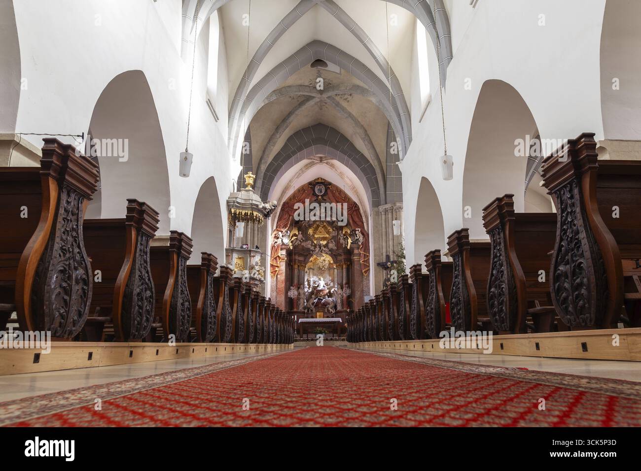Längliches Kircheninnere mit kunstvoll geschnitzten Bänken und rotem Teppich Laa an der Thaya Pfarrkirche Weinviertel Niederösterreich Österreich Stockfoto