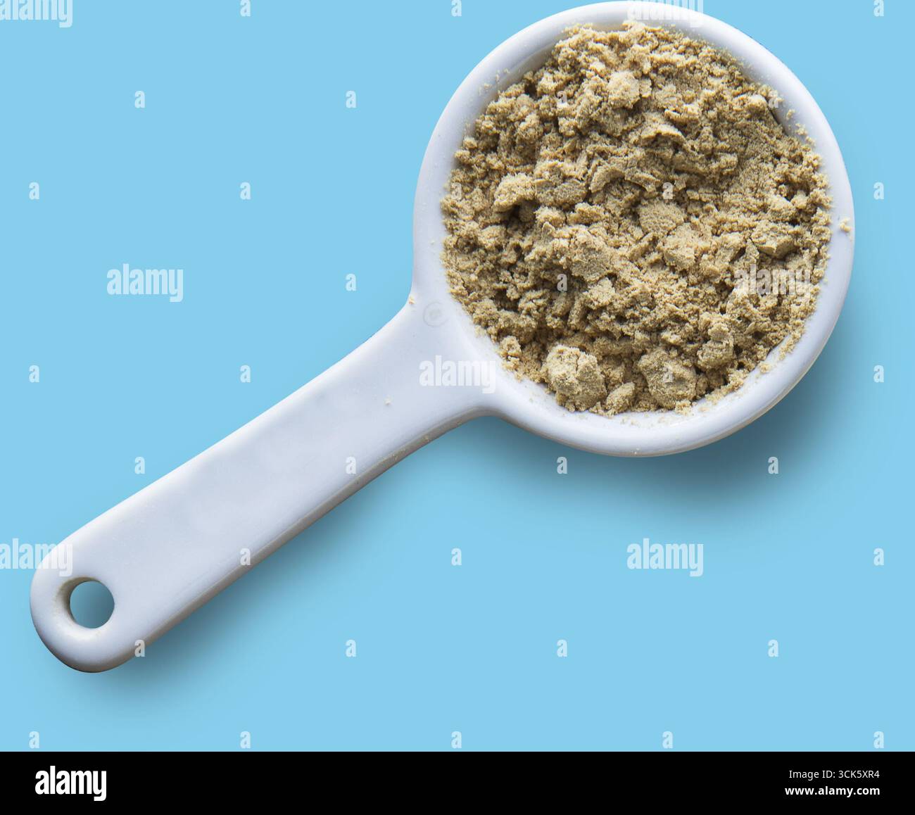 Ein weißer Messbecher, gefüllt mit einem hellbraunen Pulver, wahrscheinlich einer Lebensmittelzutat oder einem Nahrungsergänzungsmittel. Stockfoto