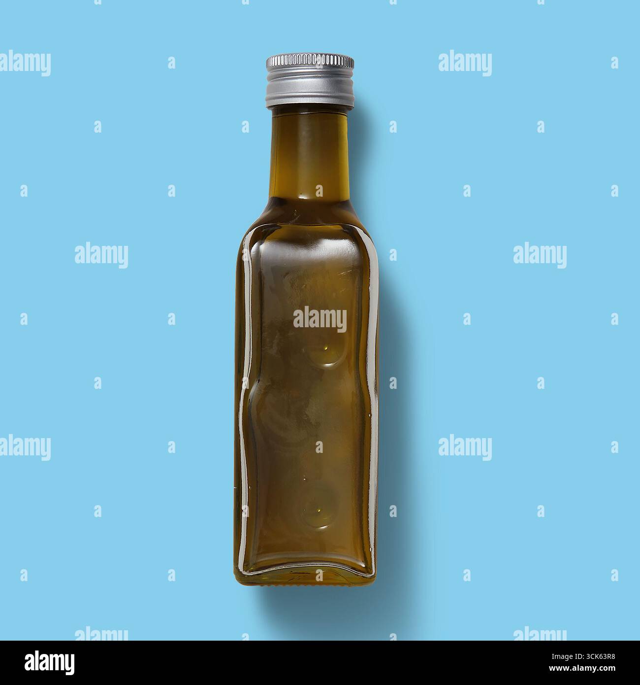 Eine Glasflasche, gefüllt mit einer goldenen Flüssigkeit, wahrscheinlich Öl, mit einem schlanken Design und einem metallischen Verschluss. Stockfoto