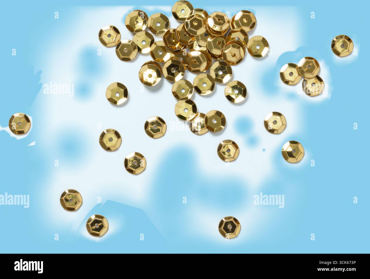 Eine Kollektion glänzender goldfarbener Pailletten, die über eine Oberfläche verstreut sind, ideal für Bastelarbeiten und dekorative Zwecke. Stockfoto