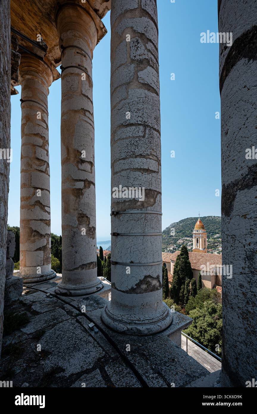 Blick durch die römischen Säulen der Trophäe der Alpen in La Turbie, Frankreich, die die Kirche von La Turbie und die umliegende Landschaft dahinter umrahmt. Stockfoto