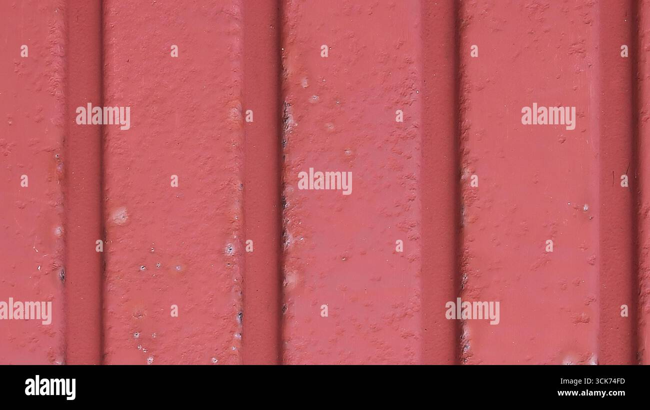 Dieses Bild zeigt eine strukturierte rote Wand mit vertikalen Linien, die ein schlichtes, aber auffälliges Design zeigt. Stockfoto