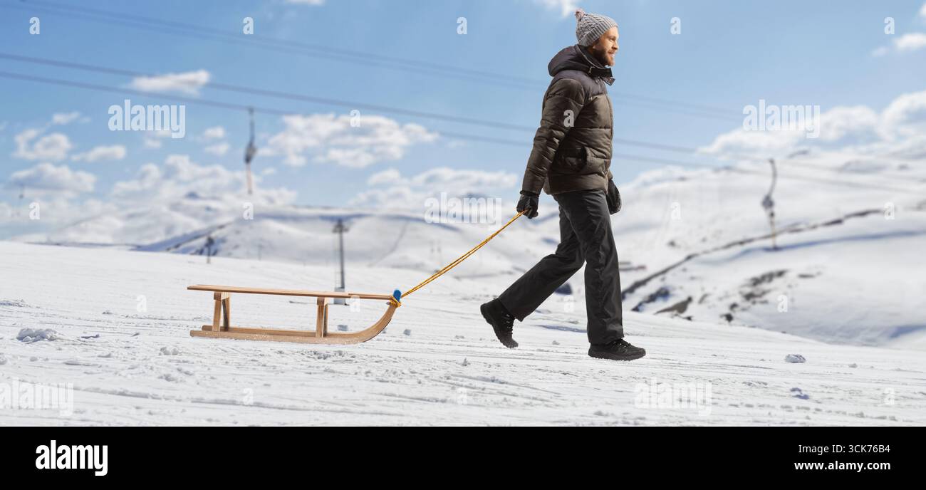 Mann, der auf einem verschneiten Berg läuft und einen Schlitten zieht Stockfoto