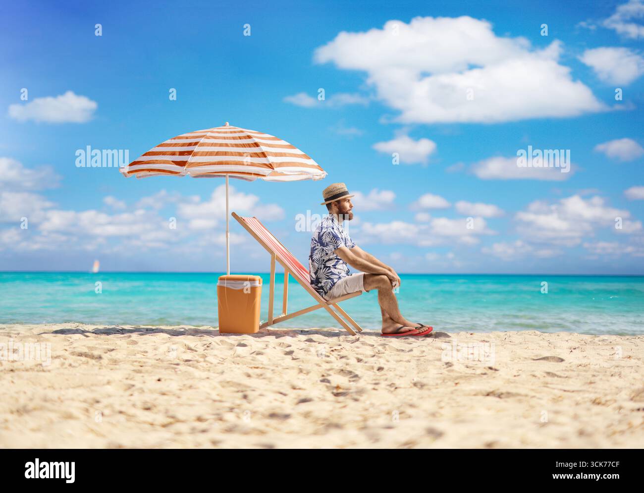 Mann, der am Meer sitzt, am Sandstrand unter Sonnenschirm Stockfoto
