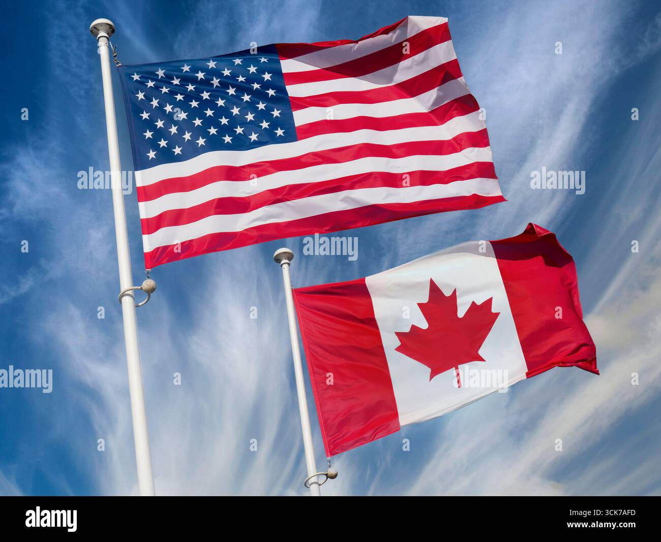 Amerikanische Flagge mit kanadischer Flagge im Wind, turbulente Wolken und blauer Himmel dahinter. Die Sterne und Streifen und die Ahornblatt-Flaggen Stockfoto