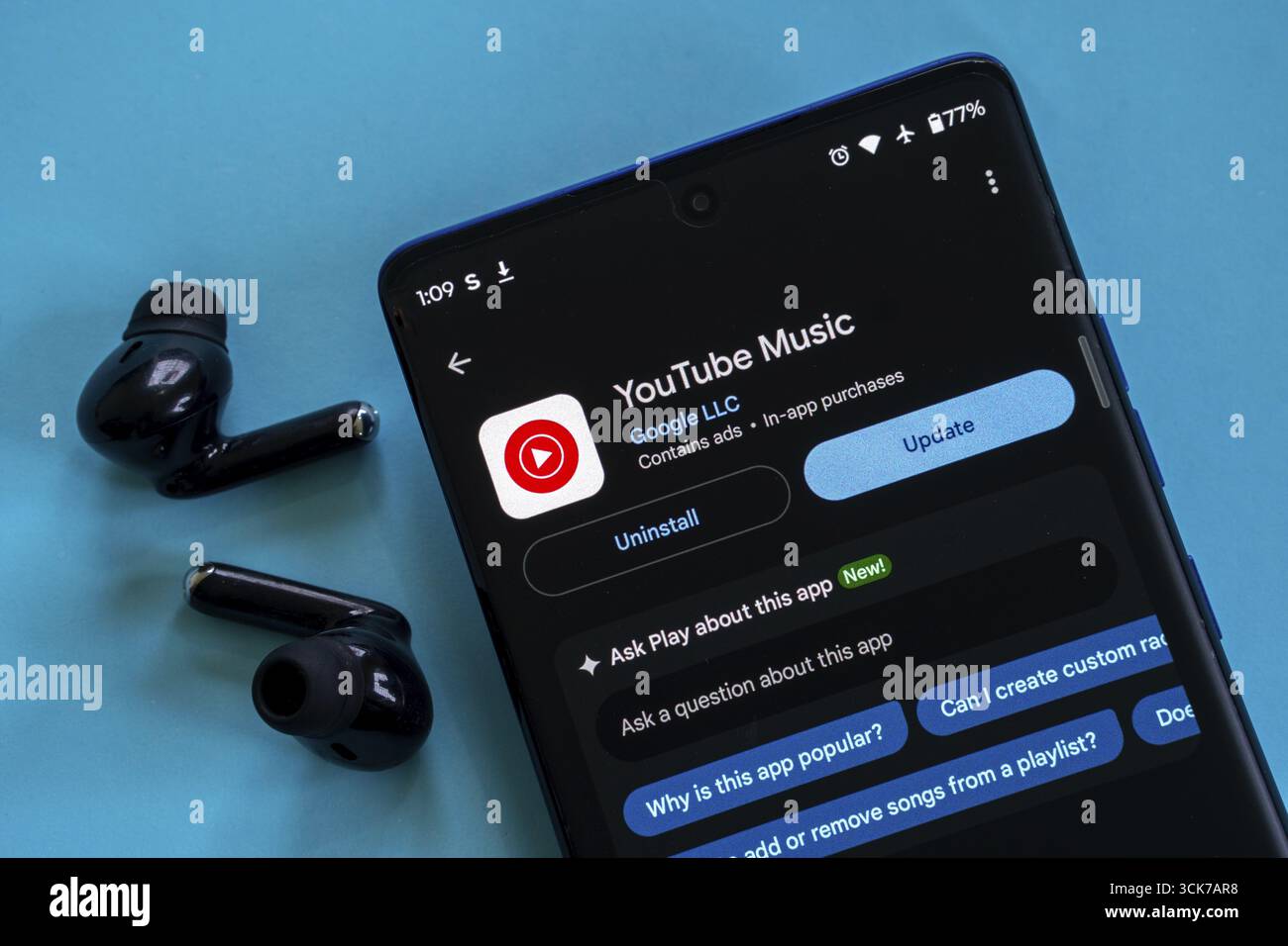 Die YouTube Music App kann auf einem Smartphone mit Ohrstöpseln auf blauer Oberfläche aktualisiert werden Stockfoto