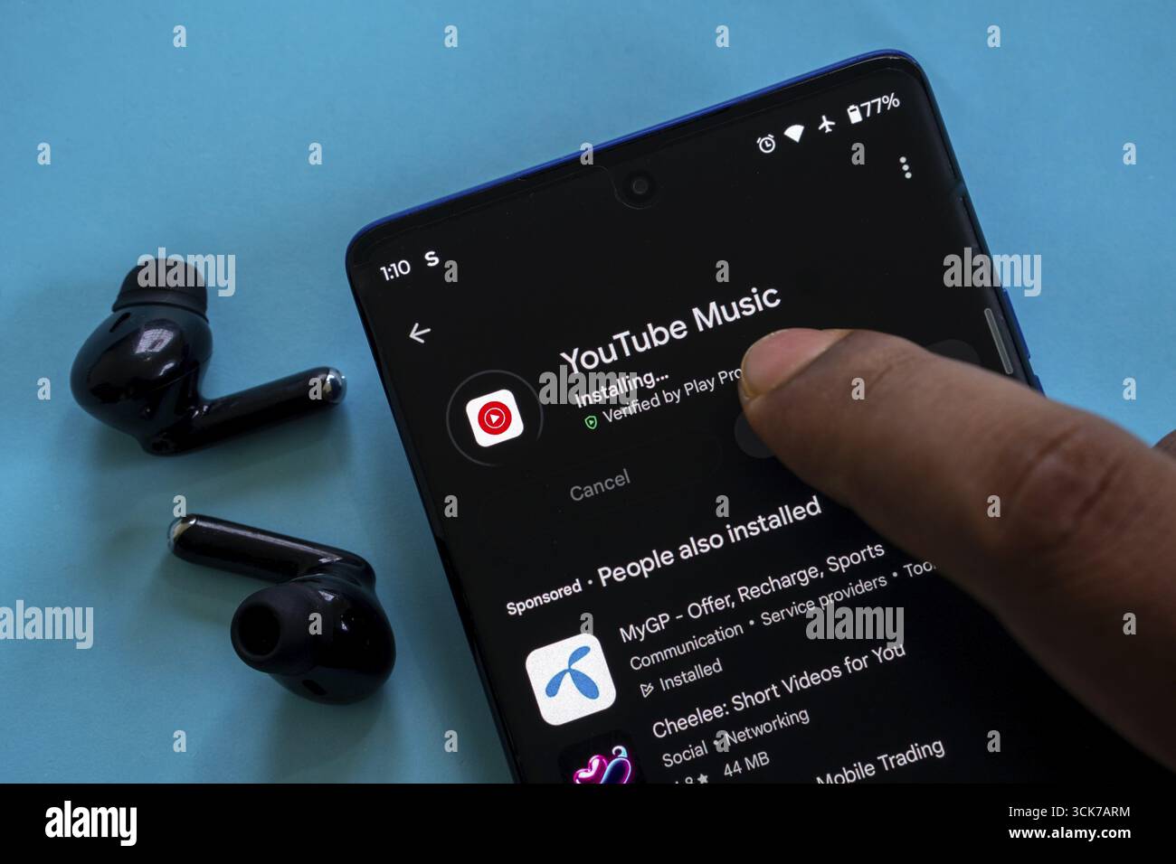 Die YouTube Music App installiert gerade auf einem Smartphone mit einem Finger und Ohrstöpseln in der Nähe Stockfoto