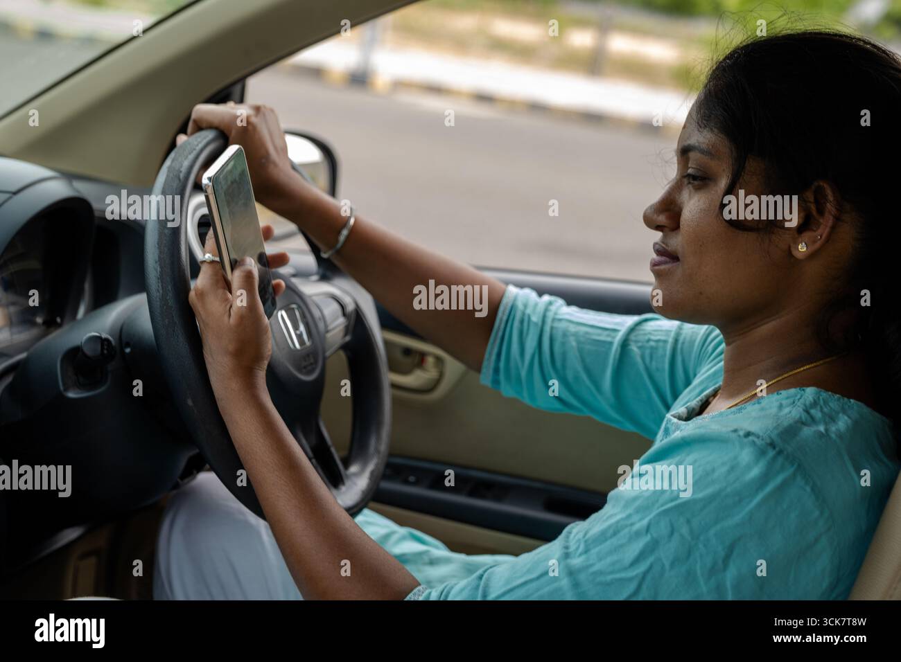 Eine junge Frau konzentriert sich auf ihr Smartphone, während sie an einem klaren Tag in einem Fahrzeug fährt, und zeigt abgelenktes Fahren. Stockfoto