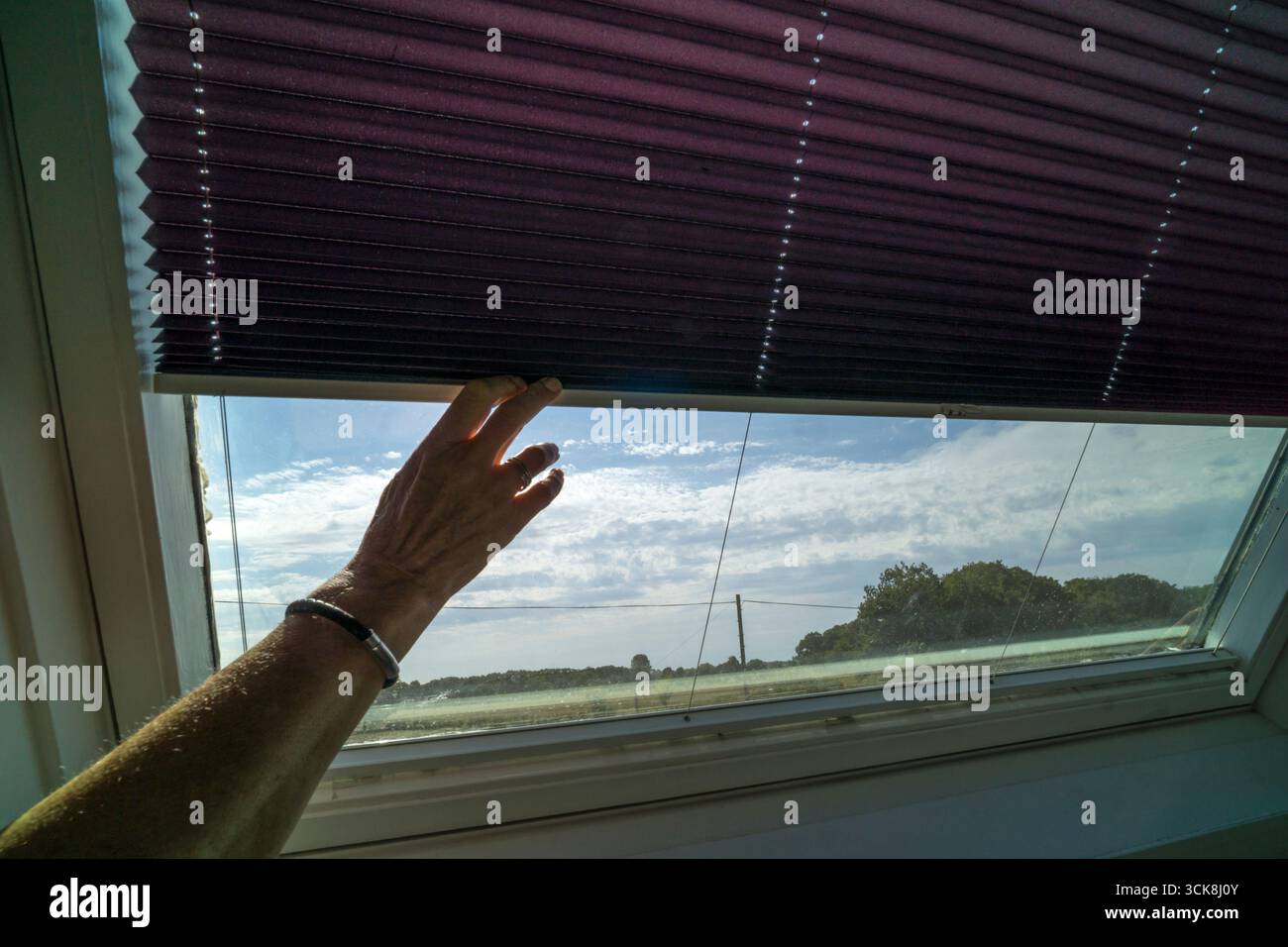 Ein Rollo auf einem Velux-Dachfenster herunterklappen, um den Raum an heißen Tagen kühl zu halten. Stockfoto