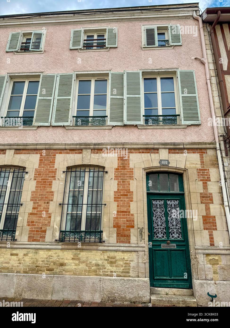 Schließen Sie die Fenster in einem historischen französischen Gebäude mit grünen Fensterläden, schmiedeeisernen Balkongeländern und verzierten Steindetails aus Ziegel und Stuck Stockfoto