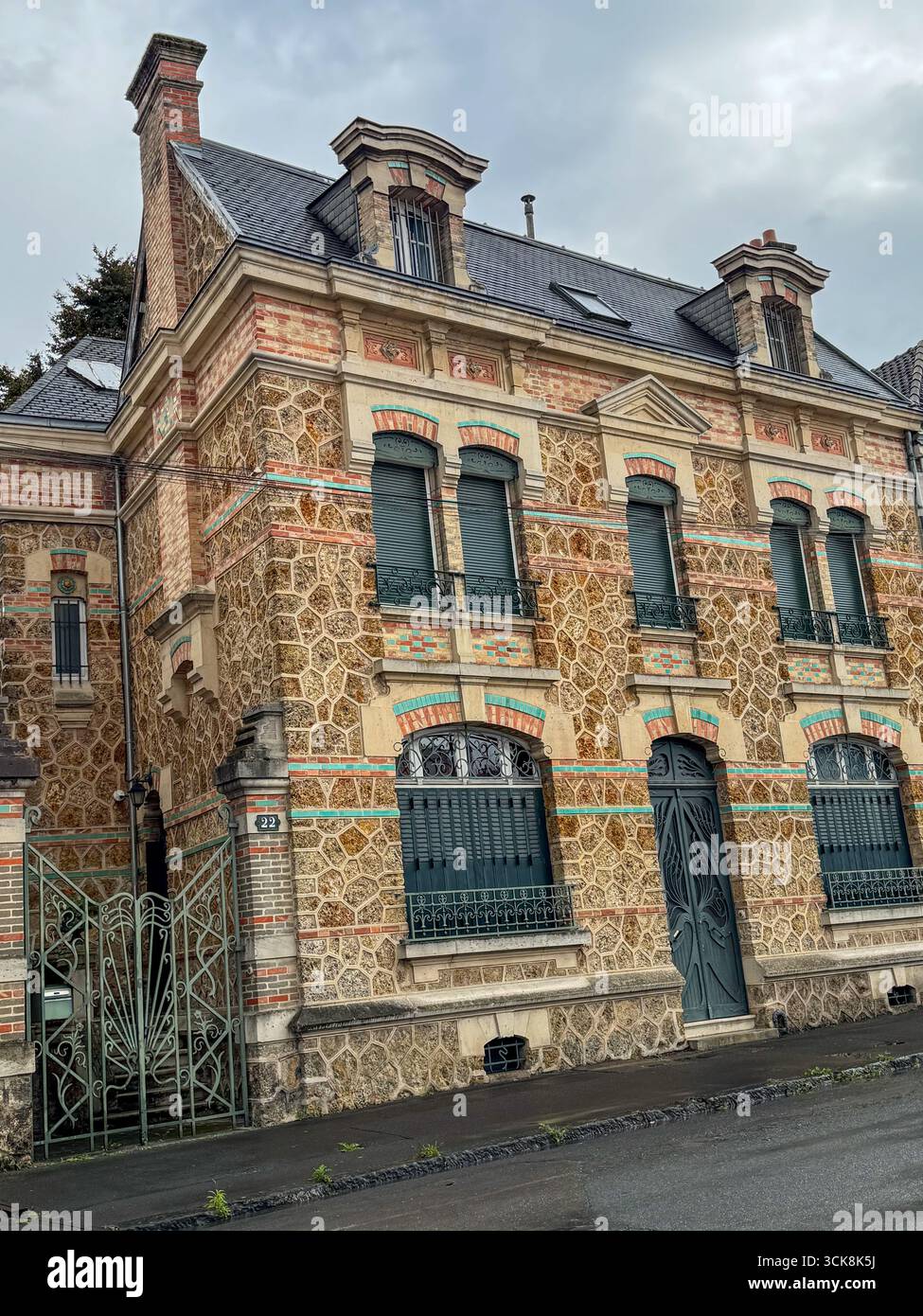 Historisches französisches Haus mit Stein- und Ziegelfassade, grünen Fensterläden, Schieferdach und regnerischer Straßenatmosphäre - Smartphone-aufgenommenes Stockfoto