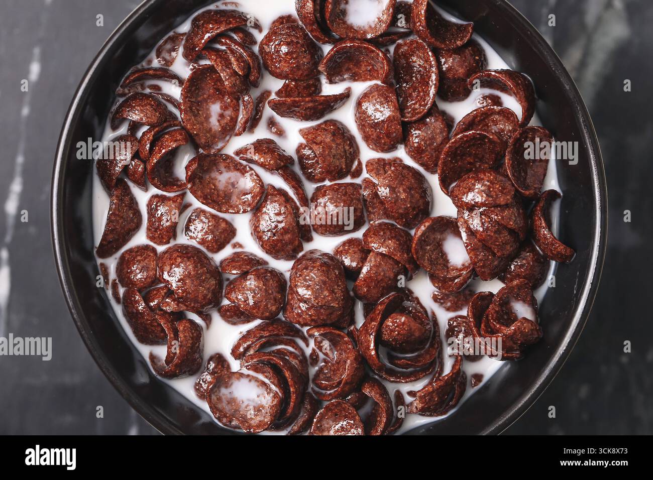 Schüssel mit Schokoladenmüsli und Milch. Zum Frühstück gab es knusprige süße Flocken. Morgenmahlzeit mit Milchernährung. Stockfoto