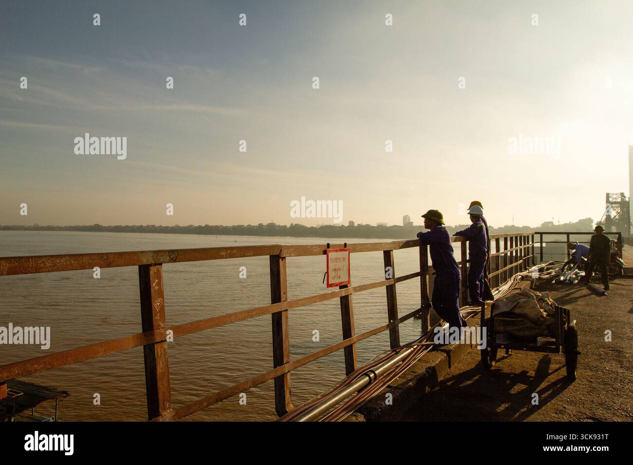 Wo-Arbeiter warten, um das Schiff zu entladen, das die Instandhaltungsteile zur langen Bienbrücke und zum Eisenbahnweg über die Brücke transportiert. Hanoi, Vietnam Stockfoto