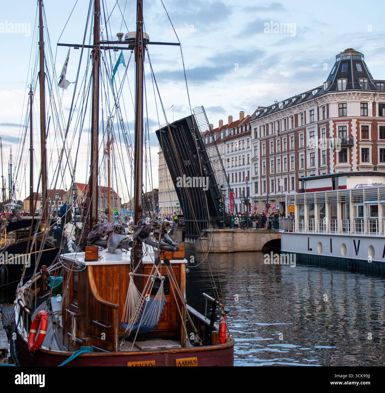 Nyhavn, Kopenhagen, Dänemark - 2. August 2025: Boote ankern in einer ruhigen Uferpromenade, da eine Brücke für vorbeifahrende Schiffe geöffnet wird. Stockfoto