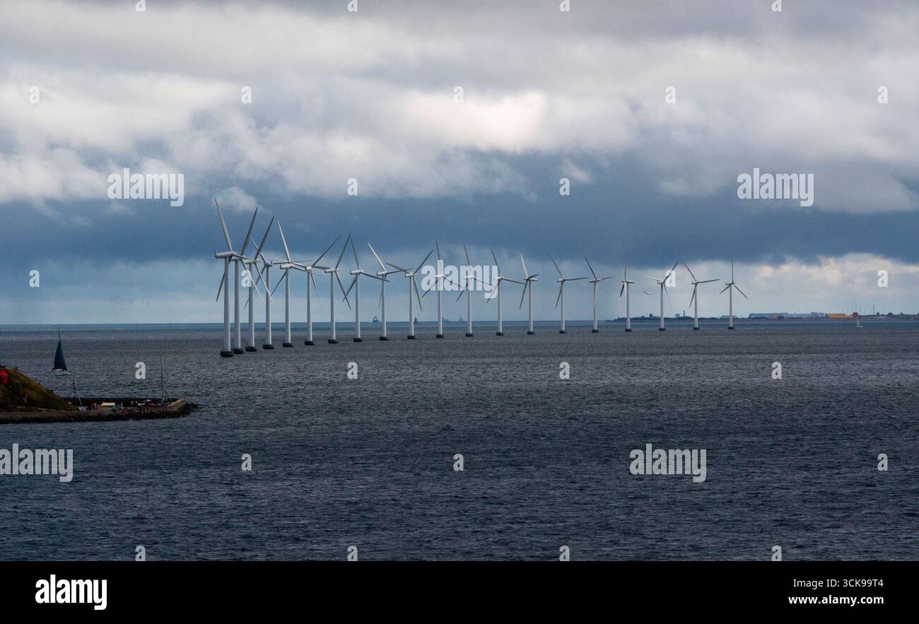Windturbinen erheben sich unter einem dramatischen Himmel in der Nähe der Küste aus dem Meer. Stockfoto