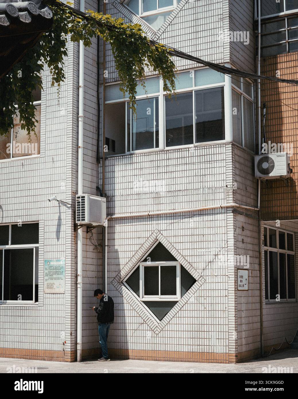Mann, der in der Nähe eines gekachelten Gebäudes mit einzigartigem geometrischem Fensterdesign in einem städtischen Gebiet steht Stockfoto